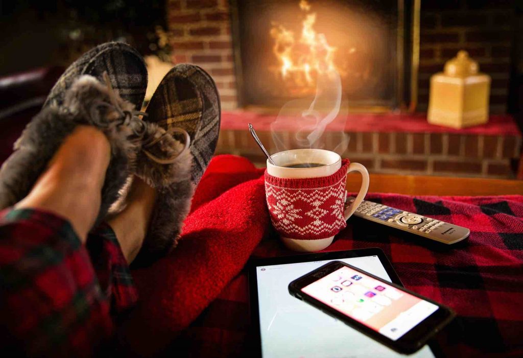 Man relaxing in slippers by the fire, with his bright phone nearby
